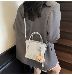 Silver bucket bag with pleated texture and cute brown bear pendant on model