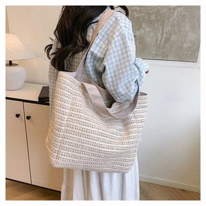 Detail of a large beige woven tote bag with a matching wide fabric strap on a model