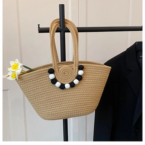 Détail d'un sac cabas en paille tissé à la main avec des pompons noirs et blancs sur le côté
