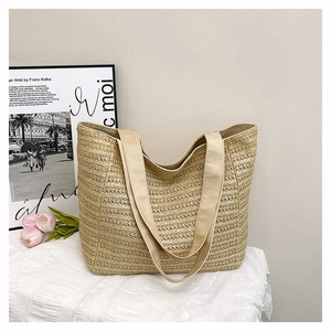 Detail of a beige woven straw tote bag with wide fabric straps on a soft white tablecloth
