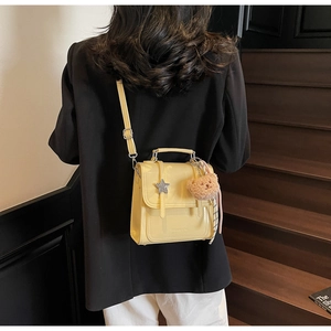 Detail of a bright yellow patent leather messenger bag with star hardware and bear charm