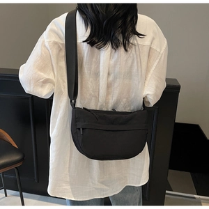 Rear view of a black nylon crescent crossbody bag with adjustable wide strap on model