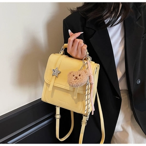 Detail of yellow mini backpack with star metal logo, plush bear, and tassel charm accessory