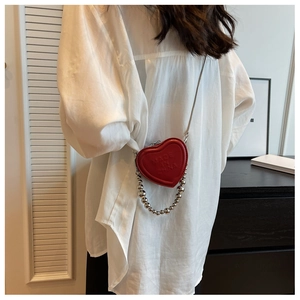 Macro detail of red heart-shaped mini purse with gold chain strap on a white shirt