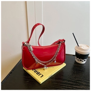 Detail of glossy red patent leather bag with silver chains and heart charms on a book