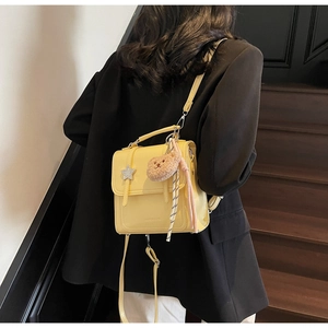 Model wearing a yellow PU leather mini backpack with a plush bear charm on wooden stairs