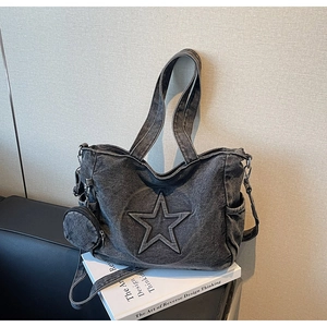Detail of grey denim tote bag with star relief, mini purse and long strap on a book