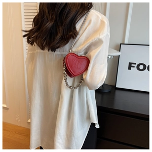 Detail view of mini red heart crossbody bag with silver chain strap on white shirt