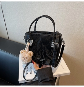 Detail of black pleated bucket bag featuring a cute plush bear charm and sleek shoulder strap