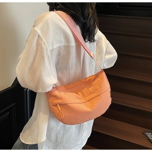 Detail of orange nylon crescent bag with woven texture and logo tag worn by a model