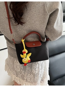 Minimalist black nylon crossbody bag with brown leather handles and a yellow duck charm