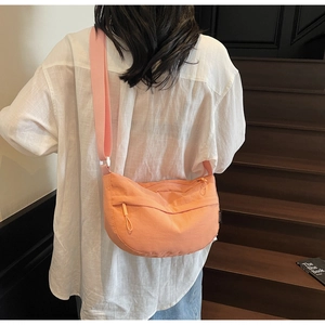 Orange-pink nylon crescent crossbody bag with wide shoulder strap shown on a model