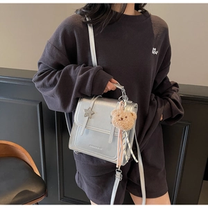 Detail showing metallic silver crossbody bag with star charm and brown plush bear pendant