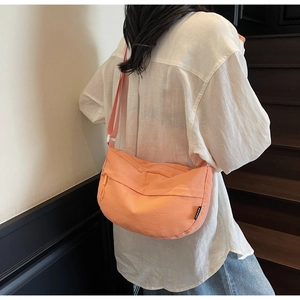 Adjustable nylon crescent bag in coral orange worn across the back by a model