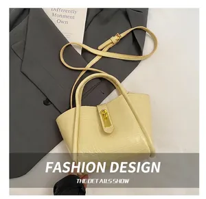Detail of beige bucket bag featuring crocodile texture, gold clasp, and adjustable strap