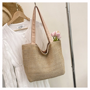 Detailed macro view of handcrafted woven straw tote bag featuring soft pink fabric straps