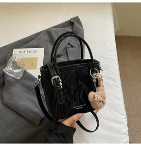 Dettaglio di una borsa a secchiello nera increspata con orsetto marrone e sciarpa a righe