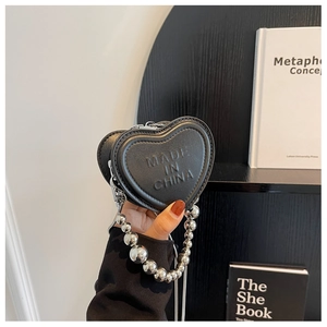 Macro shot of heart-shaped black leather mini bag with silver bead chain and embossed text