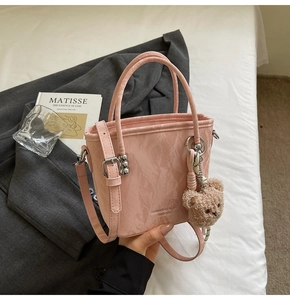 Dettaglio borsa a secchiello rosa con texture increspata, ciondolo orsetto e tracolla