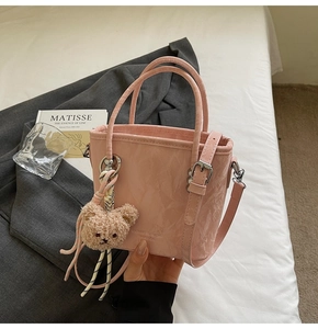 Dettaglio della borsa a secchiello rosa a pieghe con ciondolo a orsetto su letto bianco