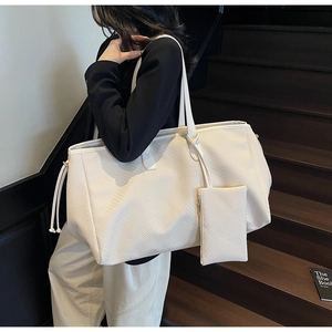 Gros plan d'un sac cabas tissé crème avec une pochette assortie porté par un mannequin
