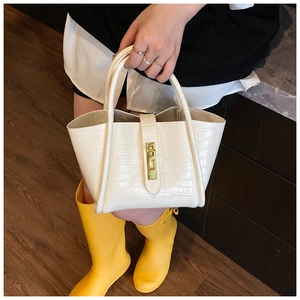Detail of white crocodile pattern bucket bag featuring a gold twist lock and ring handle