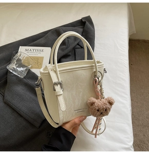 Borsa a secchiello beige con tracolla metallica e ciondolo orsetto di peluche marrone