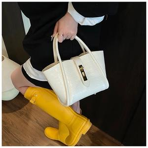 Detail of white crocodile-embossed bucket bag with golden metal twist-lock and top handle