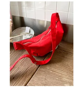 Detail of red crescent nylon crossbody bag with metal zipper on a wooden table
