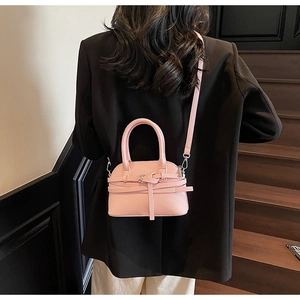 Petit sac coquille en cuir rose porté en bandoulière sur un blazer noir élégant