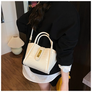 Model wearing a cream crocodile texture bucket bag with gold clasp and slim strap