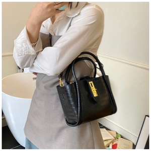 Detail of a black crocodile-embossed bucket bag with a golden turn-lock closure