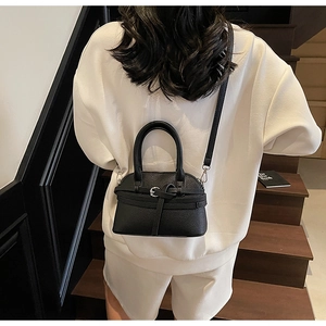 Détail d'un sac à main noir en cuir grainé avec bandoulière et poignée sur le dessus