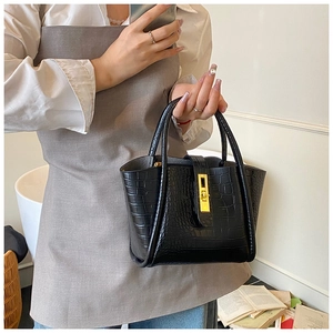 Detail of black crocodile-embossed leather tote bag with gold metal buckle and dual handles