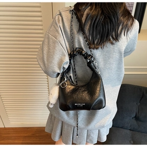 Détail d'un sac à main noir brillant avec poignée plissée et chaîne sur un mannequin