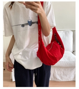 Detail of red canvas crescent bag featuring adjustable eyelet strap and woven zipper pull