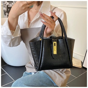 Detail of black crocodile-embossed tote bag featuring a prominent gold square twist lock