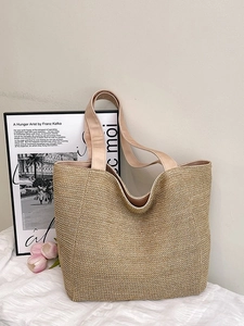 Minimalist woven straw tote bag with wide fabric shoulder straps in a stylish lifestyle setting