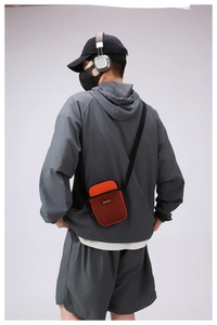 Rear view of vibrant orange crossbody phone bag with black mesh pocket on grey tracksuit