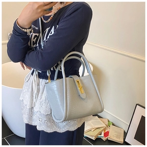Detail of light blue crocodile texture bucket bag with gold hardware held by a model