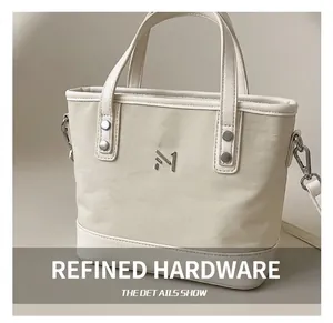 Detail shot of the polished silver metal M logo and hardware on a beige tote bag
