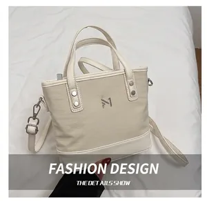 Close-up of beige canvas bucket bag with silver M logo and leather trim on grey blazer