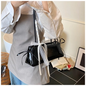 Detail of black patent leather baguette bag featuring white lace and bow accents