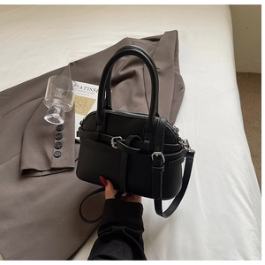 Détail d'un sac à main noir texture litchi avec boucle argentée sur un lit blanc