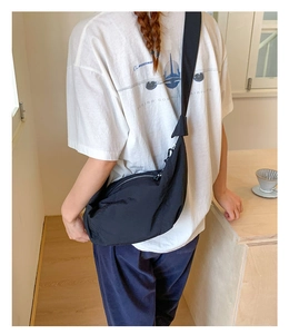 Detail of black nylon crescent crossbody bag with wide strap on a model in a cafe setting