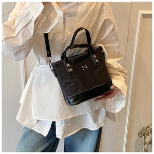 Detail of black canvas bucket bag with leather base and silver metal logo on white shirt