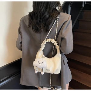 Détail d'un sac demi-lune blanc crème avec un charme nuage sur un escalier en bois