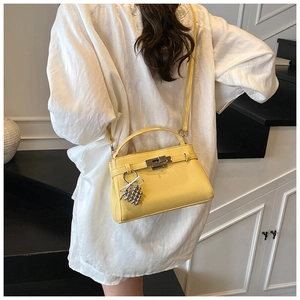 Detail of yellow lychee-textured trapezoid handbag with gold lock and grape pendant charm