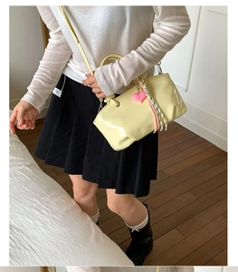 Close-up of a pale yellow glossy leather bucket bag featuring a pink heart charm