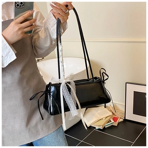 Detail of black glossy shoulder bag featuring white lace bows in a lifestyle setting